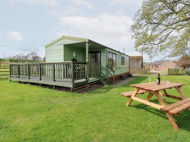 A green mobile home with a wooden deck and picnic table on a lawn at Row End farm in Brough