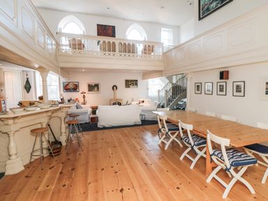 A living and dining area with a wooden table and chairs near a bar with stools and white sofas at Bethel Chapel Staithes