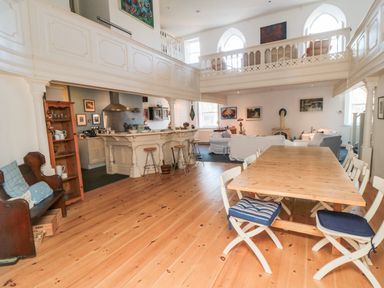 An open plan living area with wooden dining table and chairs a kitchen bar with stools and a sitting area with sofas at Bethel Chapel in Staithes