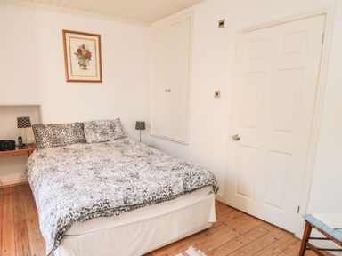 A bedroom with a bed covered in patterned bedding two bedside lamps a framed picture on the wall and a door at Bethel Chapel in Staithes