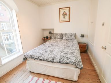 A bedroom with a bed a wooden floor two bedside tables lamps and a window at Bethel Chapel in Staithes