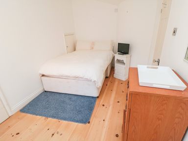 A bedroom with a bed on a blue rug a wooden dresser with a white tray and a small white nightstand with a TV at Bethel Chapel in Staithes