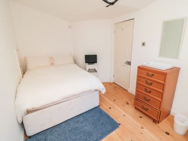 A bedroom with a double bed a small television on a white nightstand a wooden chest of drawers a mirror and a waste bin at Bethel Chapel in Staithes