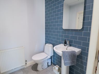 A bathroom with a white toilet a white pedestal sink with a gray towel a rectangular mirror and a blue tiled wall at Bethel Chapel in Staithes
