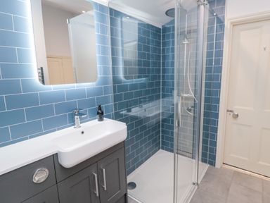 A bathroom with blue tiled walls a sink with cabinet a shower enclosure and a door at Bethel Chapel in Staithes