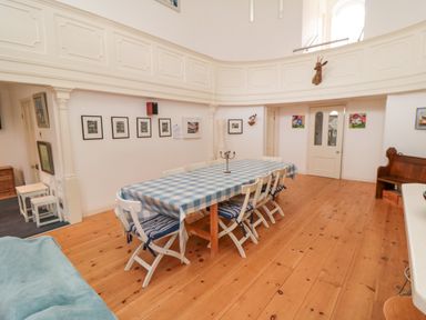 A dining room with a long table covered by a blue and white checked tablecloth and white chairs at Bethel Chapel in Staithes