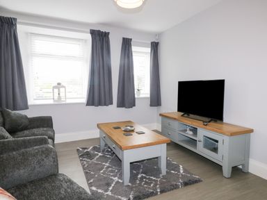 A living room with a sofa a coffee table a television and curtains at Oxen Park Farm Cottage in Oxen Park near Ulverston