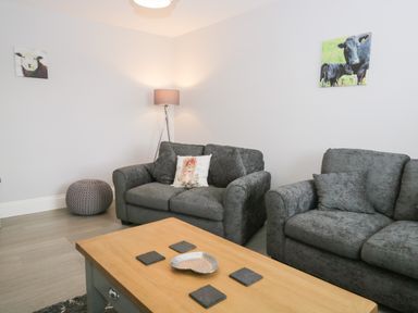 A living room with two grey sofas a wooden coffee table a floor lamp and animal pictures on the wall at Oxen Park Farm Cottage Oxen Park near Ulverston