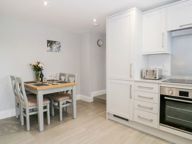 A kitchen with a dining table and four chairs next to white cabinets and a built-in oven at Oxen Park Farm Cottage Oxen Park near Ulverston