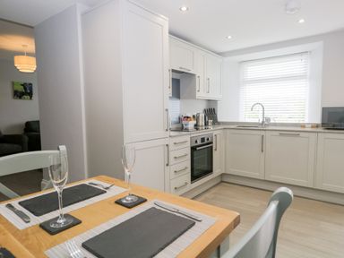 A kitchen with white cabinets a built in oven and a wooden dining table set for two at Oxen Park Farm Cottage in Oxen Park near Ulverston