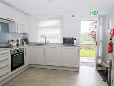 A kitchen with white cabinets a window a microwave an oven a kettle a knife set and an open door at Oxen Park Farm Cottage in Oxen Park near Ulverston