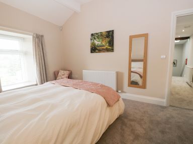 A bedroom with a bed a window with curtains a chair a wall mirror a radiator and a landscape painting at Oxen Park Farm Cottage Oxen Park near Ulverston
