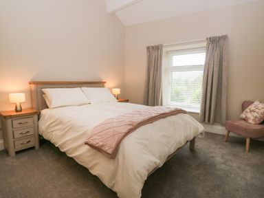 A bedroom with a double bed bedside tables lamps a window with curtains and an armchair at Oxen Park Farm Cottage Oxen Park near Ulverston