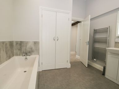 A bathroom with a bathtub, double white doors, a heated towel rail, and a white sink unit at Oxen Park Farm Cottage in Oxen Park near Ulverston