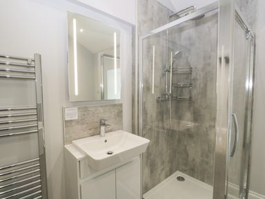 A bathroom with a sink vanity unit a mirror with lights a glass shower enclosure and a chrome towel radiator at Oxen Park Farm Cottage Oxen Park near Ulverston