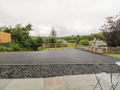 A driveway with a gravel border and a wooden fence surrounded by trees and stone walls at Oxen Park Farm Cottage in Oxen Park near Ulverston