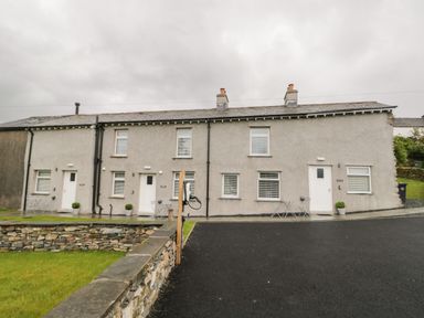 A row of three attached houses with grey exterior walls and white doors and windows at Oxen Park Farm Cottage Oxen Park near Ulverston