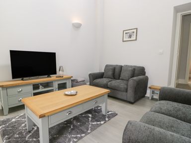 A living room with a television on a wooden cabinet a coffee table and grey sofas at Bill's Barn in Oxen Park near Ulverston