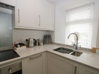 A kitchen with a corner countertop sink a set of knives a kettle and white cabinets at Bill's Barn in Oxen Park near Ulverston