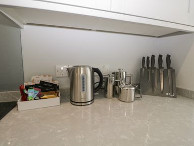 A kitchen counter with a box of coffee and tea supplies a stainless steel electric kettle a set of French presses a stainless steel teapot and a knife block with five knives at Bill's Barn in Oxen Park near Ulverston