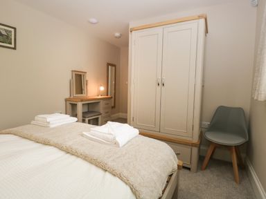 A bedroom with a bed, wardrobe, dressing table with mirror and lamp, and a chair at Bill's Barn in Oxen Park near Ulverston