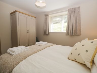 A bedroom with a wardrobe a window with curtains and a bed with pillows and towels at Bill's Barn in Oxen Park near Ulverston