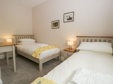 A bedroom with two single beds white bedding bedside tables lamps and framed pictures on wall at Bill's Barn in Oxen Park near Ulverston