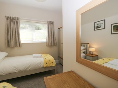 A bedroom with a single bed a yellow blanket curtains and a wardrobe at Bills Barn in Oxen Park near Ulverston