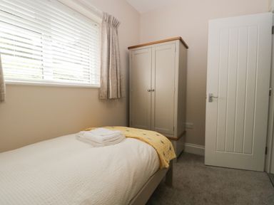 A bedroom with a single bed with folded towels and a yellow blanket a wardrobe and a window with blinds and curtains at Bill's Barn Oxen Park near Ulverston
