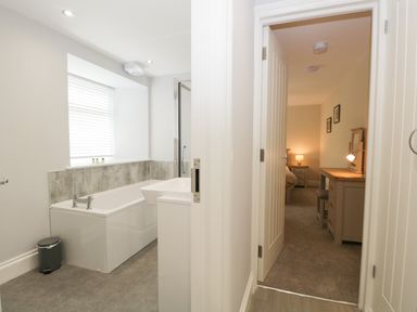 A bathroom with a bathtub and sink next to a hallway leading into a bedroom with a dressing table and lamp at Bill's Barn Oxen Park near Ulverston