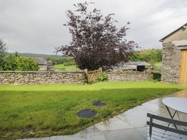 A garden with a stone wall and wooden gate overlooking fields with a purple tree near Bill's Barn in Oxen Park near Ulverston