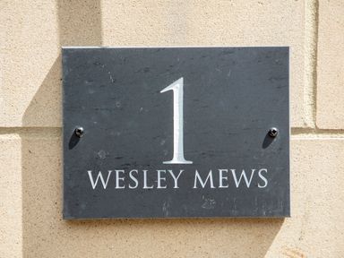 A black house number plaque with number 1 and text Wesley Mews on a beige brick wall at 1 Wesley Mews in Alnwick