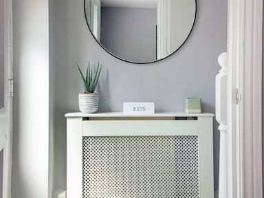 A radiator cover with a potted plant a keys box and a small container beneath a round wall mirror at 1 Wesley Mews in Alnwick