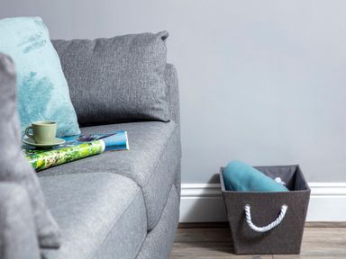 A gray couch with a blue pillow a green cup and saucer on a magazine and a gray storage basket with a blue blanket inside at 1 Wesley Mews in Alnwick