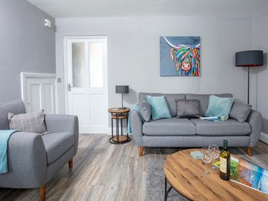 A living room with grey sofas a wooden coffee table two lamps and a colorful cow painting on the wall at 1 Wesley Mews in Alnwick