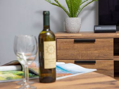 A wooden cabinet with a potted plant and a speaker on top and a wine bottle and glasses on a wooden table at 1 Wesley Mews in Alnwick