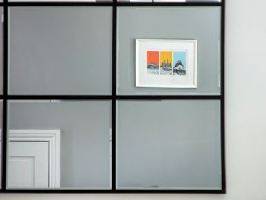 A wall with a door and a framed triptych artwork reflected in a grid mirror at 1 Wesley Mews in Alnwick
