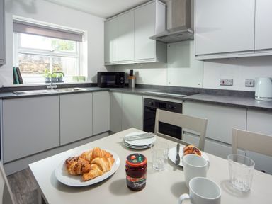A kitchen with white cabinets gray countertops a microwave oven and a table with croissants jam and cups at 1 Wesley Mews in Alnwick
