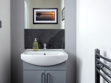 A bathroom sink with a soap dispenser above a gray cabinet and a framed picture on the wall at 1 Wesley Mews in Alnwick