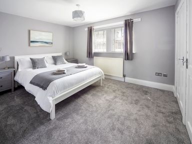 A bedroom with a bed side tables lamps and a window with curtains at 1 Wesley Mews in Alnwick
