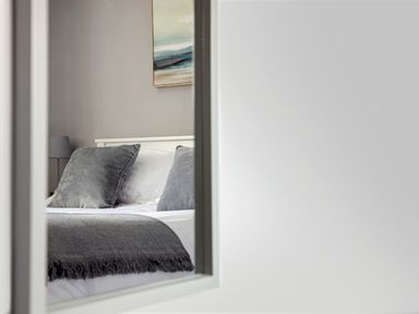 A bedroom with a bed, gray pillows, a gray throw blanket, a painting on the wall and a lamp at 1 Wesley Mews in Alnwick