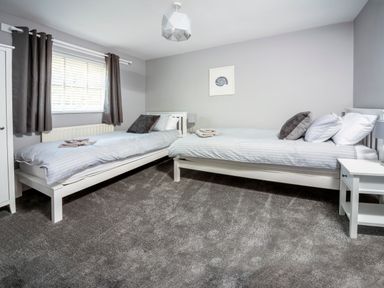 A bedroom with two single beds bedside tables a window with curtains and a wardrobe at 1 Wesley Mews in Alnwick