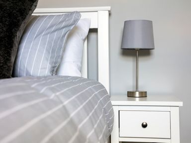 A bed with striped bedding and pillows next to a nightstand with a lamp at 1 Wesley Mews in Alnwick