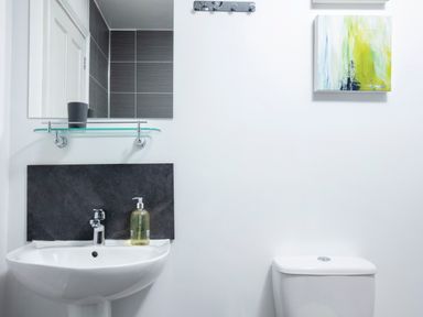 A bathroom with a white sink and soap dispenser next to a white toilet with a colorful painting on the wall at 1 Wesley Mews in Alnwick