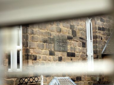 A stone building with a sign reading Wesleyan Chapel 1786 and tall white windows at 1 Wesley Mews in Alnwick