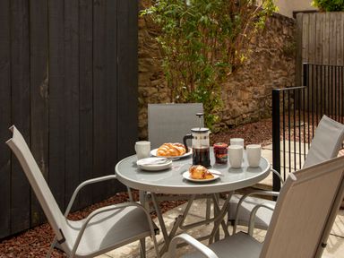 An outdoor patio with a round glass table set with croissants a French press coffee maker mugs and jam at 1 Wesley Mews in Alnwick