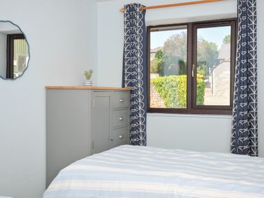 A bedroom with a bed, window, cabinet, and mirror at Columbine Cottage in Bude