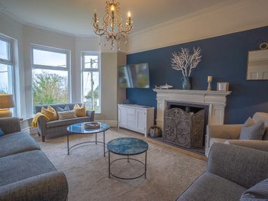 A living room with sofas a fireplace a mounted TV and large windows at Argoed in Abersoch