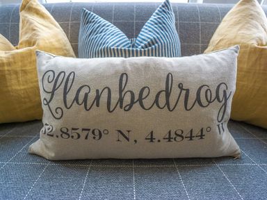A sofa with grey checkered fabric and pillows including one with Llanbedrog and coordinates printed on it at Argoed in Abersoch