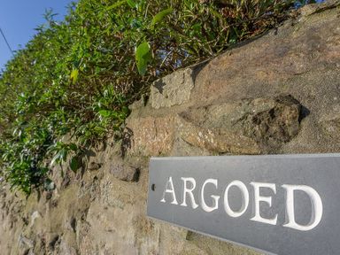 A stone wall with green foliage and a sign that says Argoed at Argoed in Abersoch